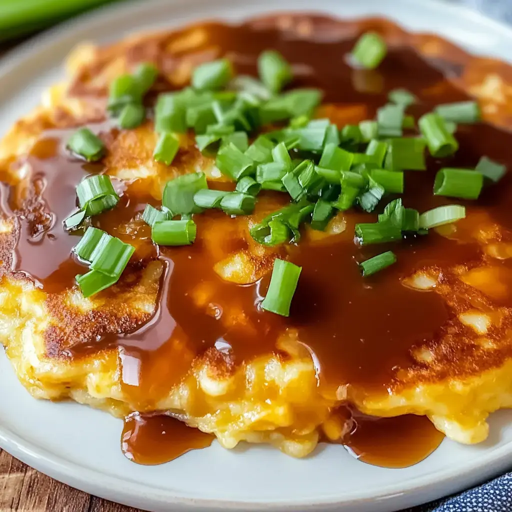 A fluffy golden omelet drizzled with savory sauce, finished with fresh green onions, on a white dish.