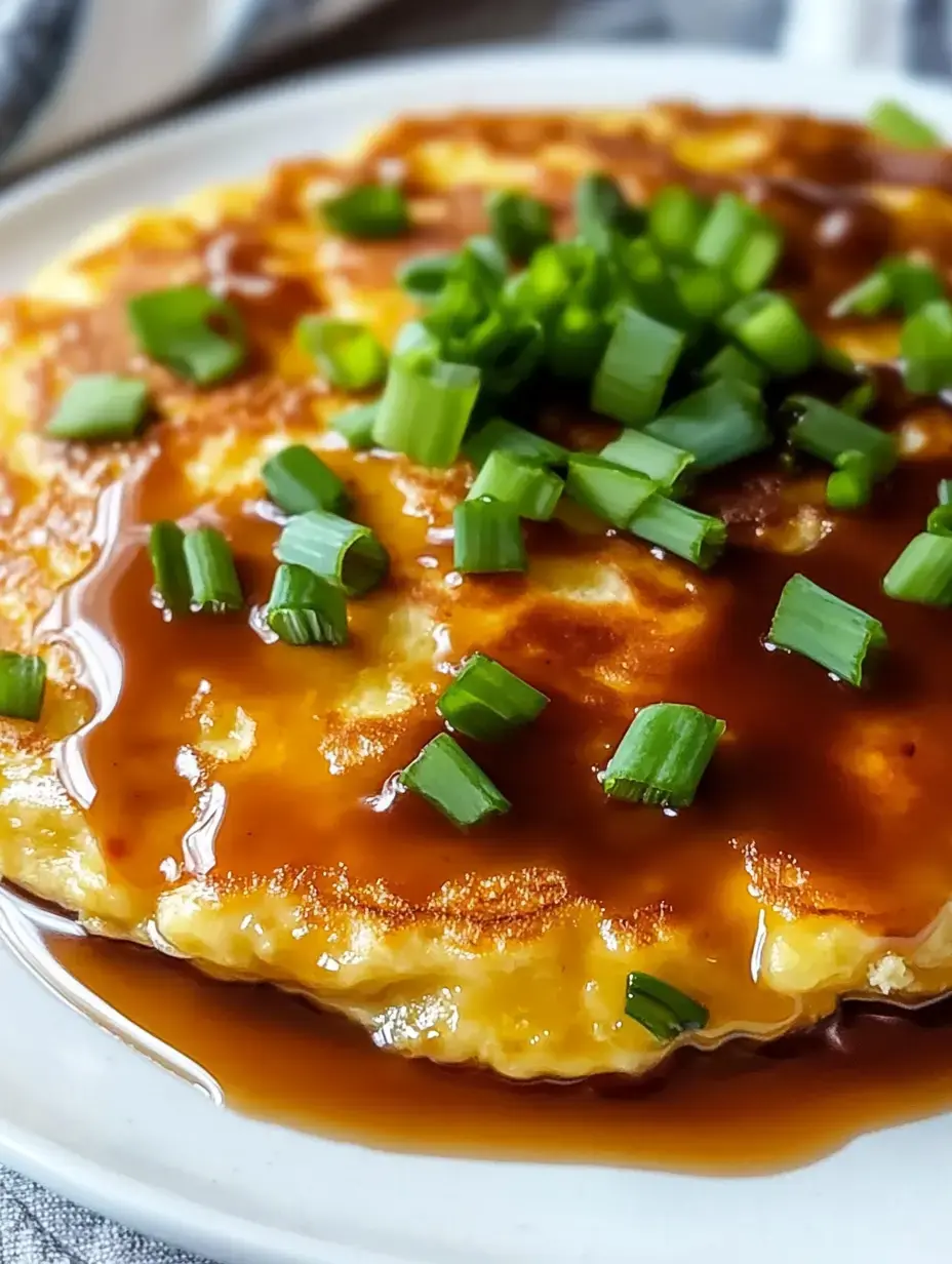 A close-up of a savory pancake topped with chopped green onions and drizzled with a brown sauce, served on a white plate.