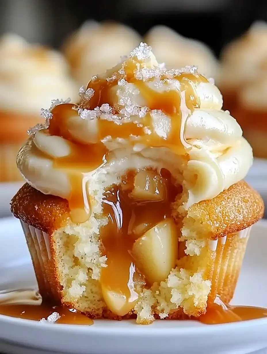 A freshly baked cupcake with creamy frosting and caramel dripping down, revealing a soft center filled with apple chunks.